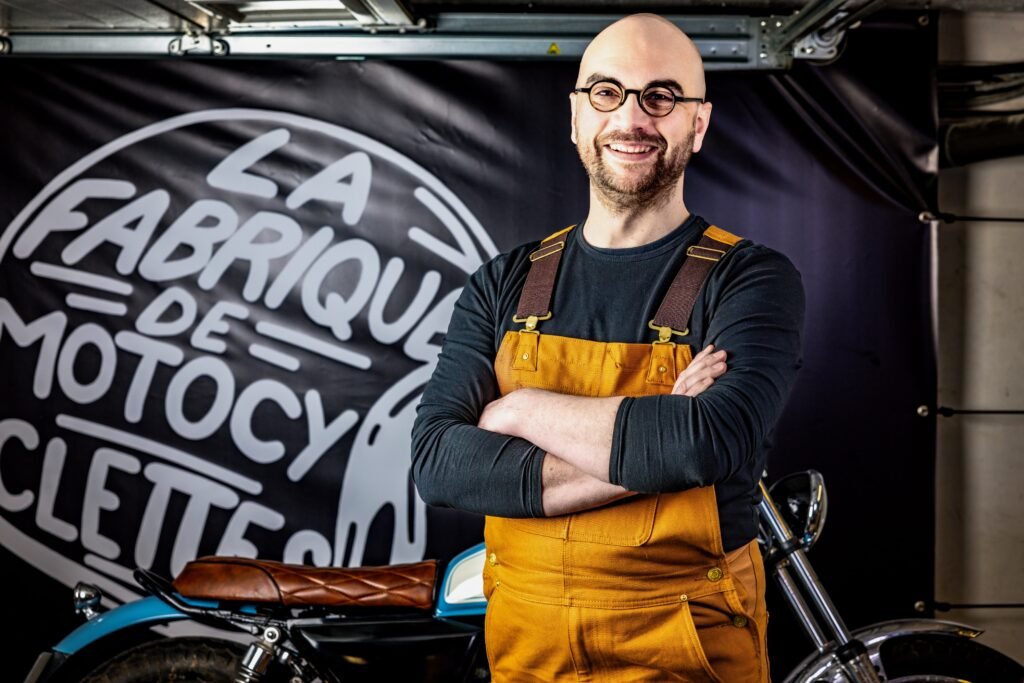 homme en salopette jaune à lunettes devant une moto