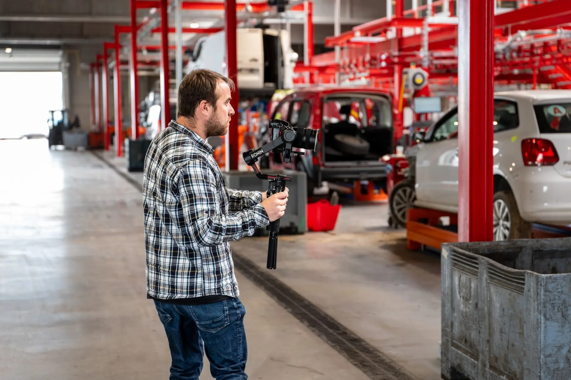 homme tenant une camera à la main dans un garage avec des véhicules
