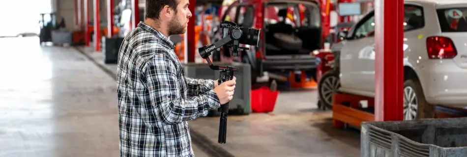homme tenant une camera à la main dans un garage avec des véhicules